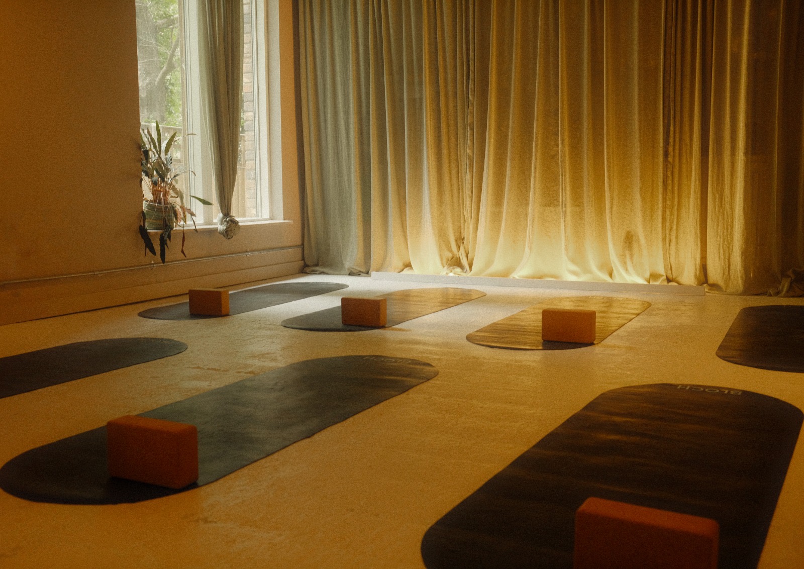 A warm, sunlit studio with yoga mats and amber blocks laid out, soft curtains diffusing golden light